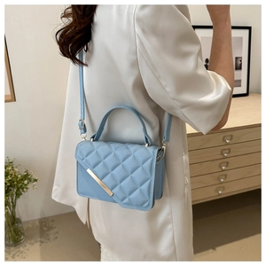 Detail of light blue quilted crossbody bag with golden metal bar and elegant handle