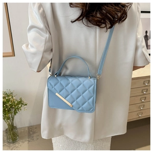 Close-up of light blue quilted crossbody bag with gold metal trim worn by model
