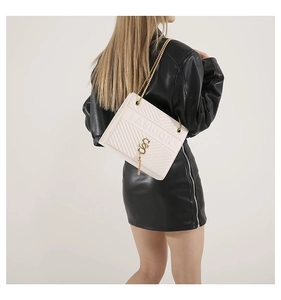 Detail of white quilted crossbody bag with gold chain strap and metal tassel on model