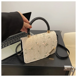 Detail of straw woven handbag with pink floral embroidery and black top handle