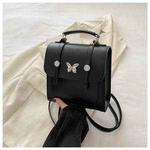 Detail of a black square crossbody bag featuring a silver butterfly buckle and matte leather