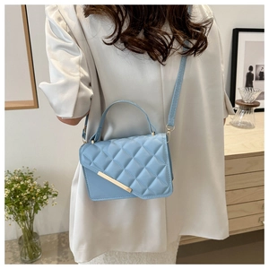 Detail of light blue quilted crossbody bag with gold metal trim and asymmetrical flap