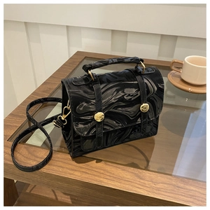 Détail du sac à main noir texture marbre avec boucles dorées sur table en bois
