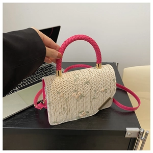 Detail of hand-woven straw crossbody bag with floral embroidery and pink handles