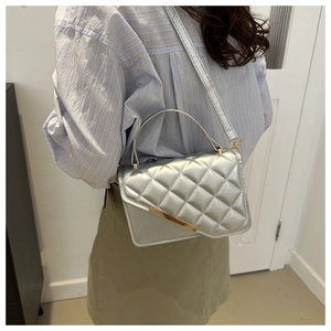 Detail of silver quilted handbag with golden metallic frame and adjustable strap on a model