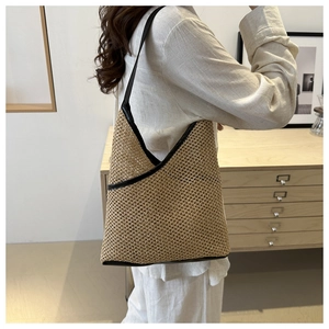 Detail of a large woven straw bucket bag with black leather shoulder strap on a model