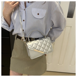 Detail view of silver quilted crossbody bag with gold metal trim and top handle