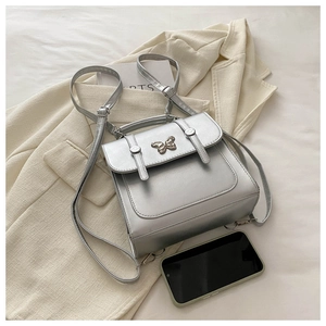 Silver mini backpack with butterfly buckle placed on a beige blazer with lifestyle items