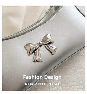 Detail of silver metallic baguette bag featuring a polished bow ornament and matte finish