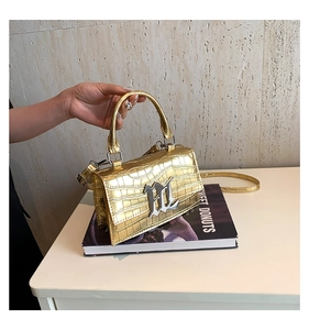 Detail of gold faux crocodile texture and metallic logo on chic square handbag