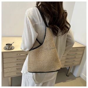 Detail of handwoven straw shoulder bag with black contrast trim on a beige textured body