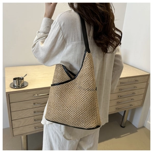Detail of hand-woven straw tote bag with black leather trim and slender shoulder strap