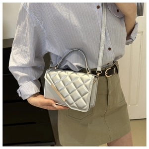Detail of silver metallic quilted handbag featuring a gold bar accent and top handle