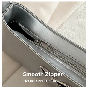 Macro detail of silver leather bag showing smooth metal zipper and silver bow decoration