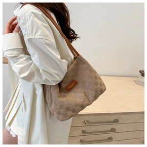 Detail of tan suede shoulder bag featuring large embossed checkered pattern and logo tag