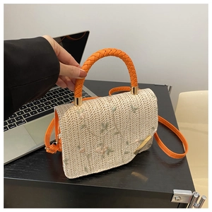 Detail of floral embroidery and orange woven handle on the beige straw square handbag