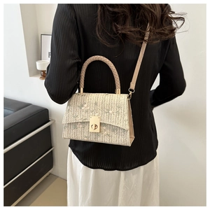 Close-up of cream woven bag with green floral embroidery and gold metal clasp detail