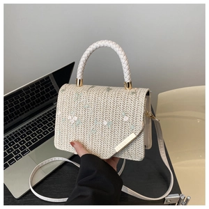 Close-up of beige woven straw handbag featuring delicate floral embroidery and metal detail