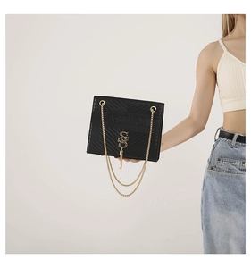 Detail of black V-quilted leather bag with gold metal logo and fringe chain strap