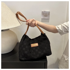 Detail of black woven checkerboard tote bag with premium brown leather strap and brand logo