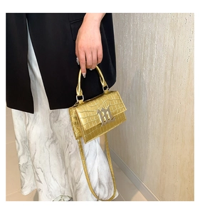 Detail of gold crocodile embossed leather handbag with metallic clasp and chain strap