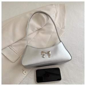 Close-up of a silver metallic hobo bag with a decorative metal bow on a textured background