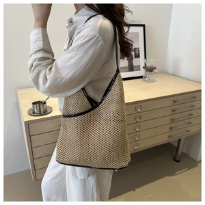 Detail of hand-woven straw shoulder bag featuring black leather trim and V-shaped opening