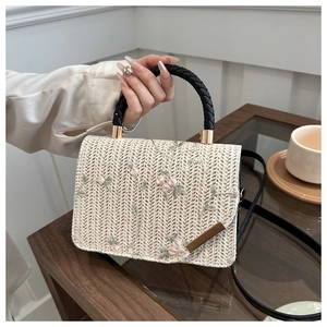 Detail of straw handbag with floral embroidery, black handle and woven shoulder strap