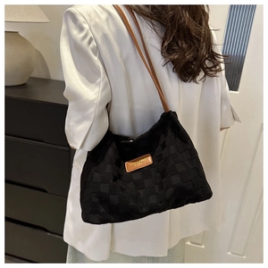 Detail view of black checkerboard hobo bag with brown leather strap and brand label