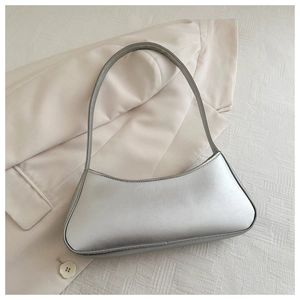 Flat lay of a silver metallic crescent underarm bag on a beige blazer background