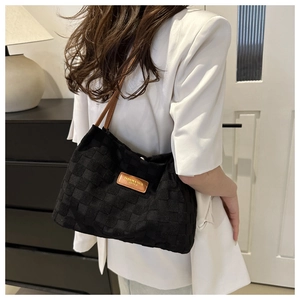 Detail of black woven checkerboard tote bag with brown leather straps and metal brand plate