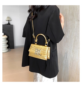 Detail of metallic gold crocodile pattern handbag with metal letter logo on structured flap