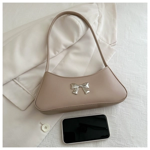 Close-up of beige shoulder bag with silver bow detail and a phone for size reference