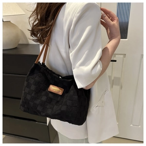 Detail of black woven shoulder bag with brown leather tag shown on a white blazer