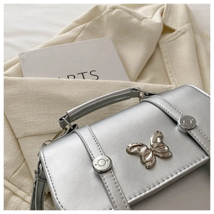 Detail of silver metallic butterfly flap bag with polished metal studs and stitching