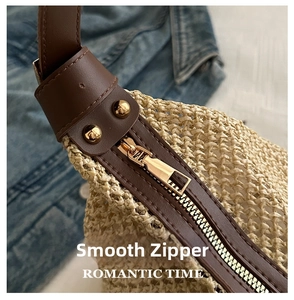 Detail of straw tote bag showing smooth metal zipper and brown leather shoulder strap