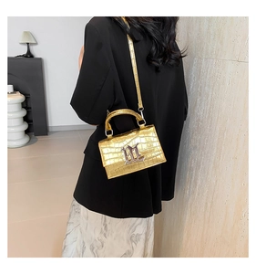 Detail of metallic gold crocodile pattern handbag with silver M logo and shoulder strap