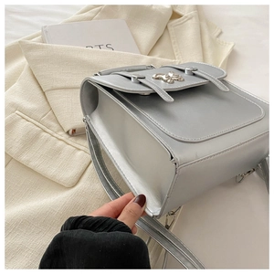 Detail of silver metallic crossbody bag featuring double buckle straps and metal bow