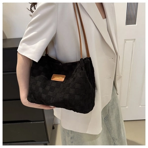 Detail of black checkered woven tote bag with brown straps styled on a white blazer