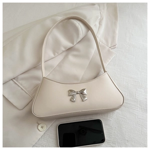 Close-up of cream beige bow shoulder bag with silver hardware and phone for size comparison