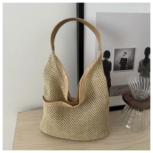 Détail du sac seau en maille tissée avec bandoulière en cuir sur une table en bois