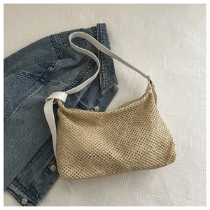 Detail of woven straw shoulder bag with adjustable white leather strap on denim background