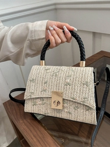 Straw handbag with floral embroidery and black leather handles shown in a lifestyle setting