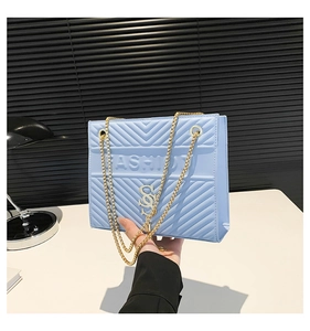 Detailed view of light blue quilted crossbody bag with golden chain strap and fashion logo