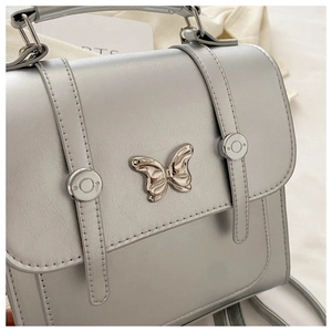 Detail of silver crossbody bag featuring butterfly metallic hardware and buckle straps