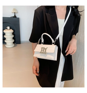 Detail of white crocodile pattern square bag with metal logo and sleek top handle