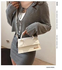 Close-up of white leather handbag featuring gold metal logo and crossbody strap detail