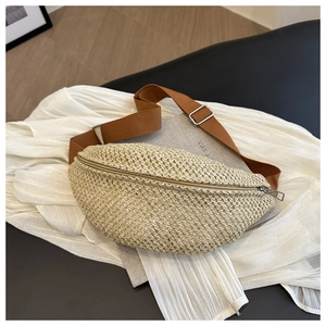 Detailed view of woven straw chest bag with brown canvas strap and natural texture