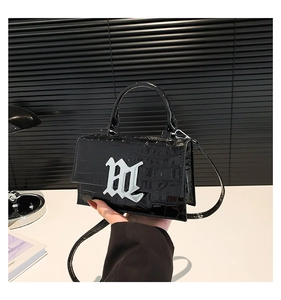 Detail of black crocodile texture bag with gothic logo and glossy finish
