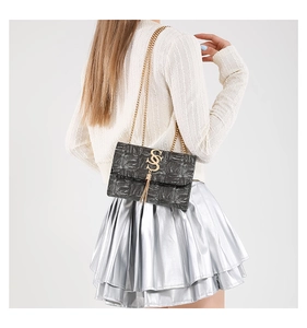 Gros plan du sac à chaîne noir texture crocodile avec logo doré et pompon sur modèle